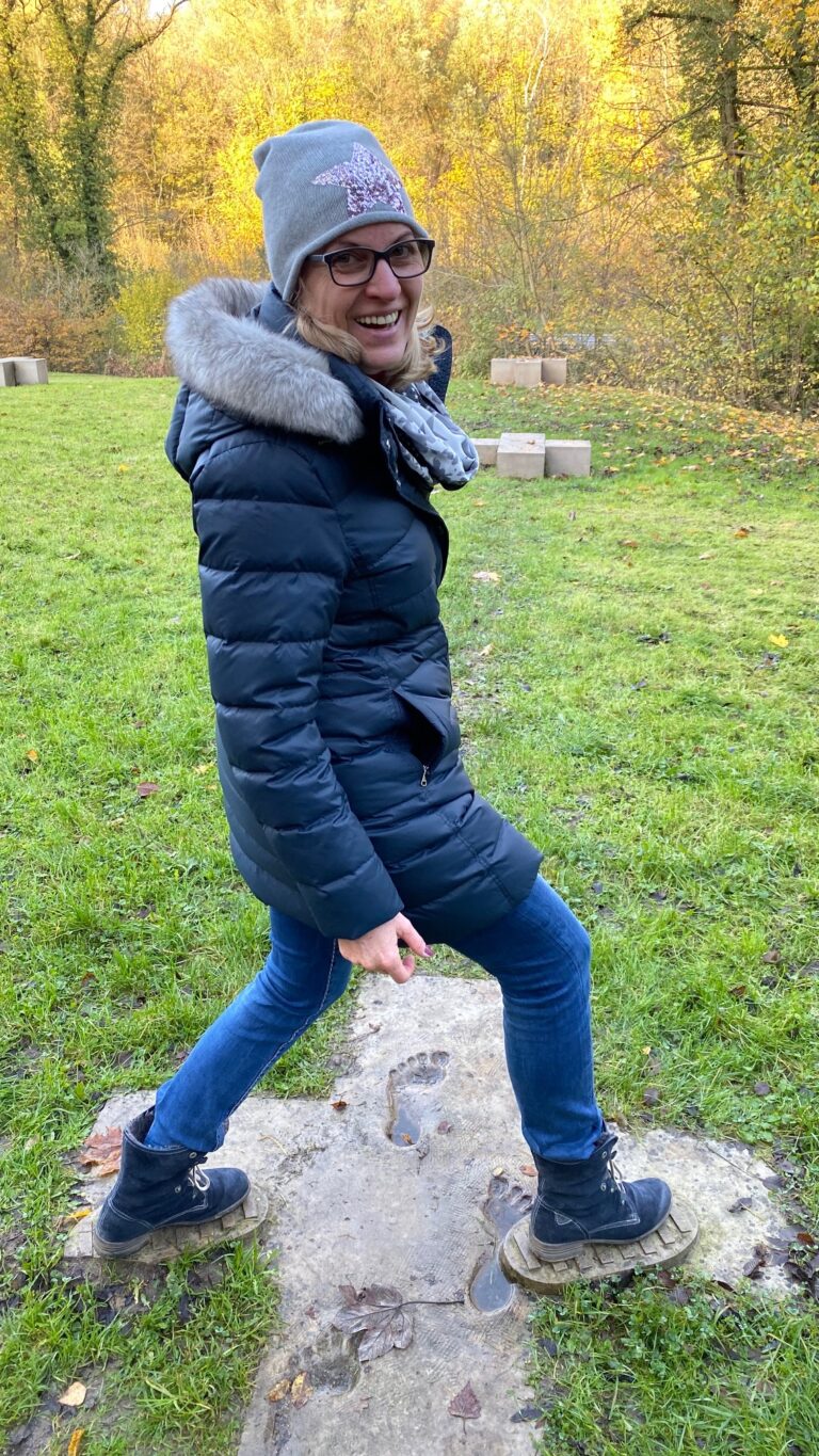 Yvonne Heckmann steht in einem Park und trägt eine blaue Jacke und eine graue Wollmütze mit Glitzer-Stern.